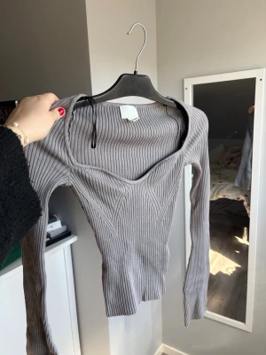 Grå ribbad långärmad topp - Snygg grå ribbad topp med lång ärm och markerad v-ringning. Figurnära passform och stretchigt material som ger en modern look. Perfekt att styla med jeans eller kjol för en trendig outfit. Aldrig använd ❣️