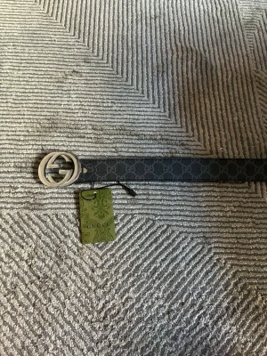 Svart Gucci bälte med GG-spänne - Snyggt svart bälte från Gucci med det klassiska GG-mönstret längs hela bandet och ett stort, silverfärgat GG-spänne. Perfekt accessoar för att lyfta vilken outfit som helst. Kommer med originaltagg. Gjort 2 extra hål.