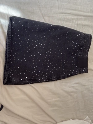 Jeanskjol  - Säljer en svart kort jeanskjol  med glittriga prickar över hela tyget. Kjolen har en rak passform och dragkedja bak. Perfekt att styla med en enkel topp eller hoodie för en chill look.