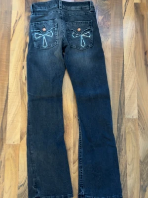Mörkblå jeans med rosetter från Gina Tricot - Snygga mörkblå jeans från Gina Tricot med raka ben och broderade rosetter på bakfickorna. Jeansen har klassisk femficksmodell och kopparfärgade knappar. Perfekta för dig som vill ha en unik detalj på dina jeans.