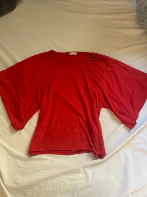 Röd topp med vida ärmar från cubus - Snygg röd topp från cubus med vida, korta ärmar och rund halsringning. Tillverkad i mjuk bomull som känns skön mot huden. Perfekt för dig som vill ha en enkel men ändå statement topp i garderoben.