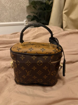 Louis Vuitton neccesär - Säljer en Louis Vuitton handväska i klassiskt brunt monogrammönster med guldfärgade detaljer🤍 Kopia med lite slitage 