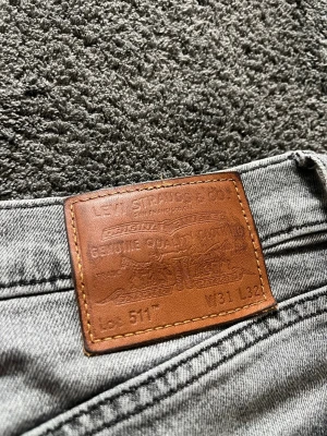 Grå Levi's 511 slim jeans - Snygga grå Levi's 511 jeans med klassisk femficksdesign och dragkedjegylf. Jeansen har en modern, smal passform och är tillverkade i mjukt denimtyg. Perfekta för en avslappnad och trendig stil. Precis ovanför högra bakre fickan har det gått upp ett litet hål, men det går ju att sy om man vill det