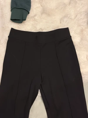 Svarta kostymbyxor från H&M - Snygga svarta kostymbyxor från H&M med hög midja och pressveck framtill. Byxorna har en stilren och rak passform som ger en clean look. Perfekta för dig som vill ha en klassisk men modern stil. Materialet känns mjukt och följsamt.