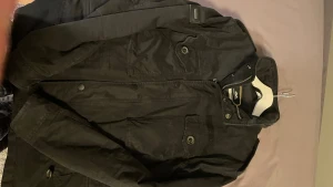 Svart jacka från superdry - Säljer en svart jacka från Mountain Works med flera fickor, hög krage och både dragkedja och knappar framtill. Jackan har lång ärm och en klassisk, stilren look som passar perfekt till kyligare dagar.