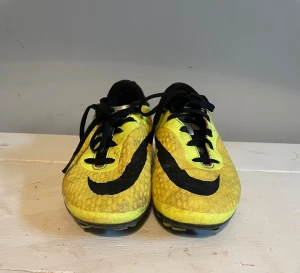Nike Hypervenom gula fotbollsskor - Säljer ett par Nike Hypervenom fotbollsskor i en riktigt schysst gul färg med svarta detaljer och snörning. Skorna har en låg profil och mönstrad ovansida för bättre bollkontroll. Yttersulan har fasta dobbar som passar perfekt för spel på gräs.