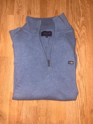 Blå halvzip tröja från Lexington - Snygg blå tröja från Lexington med halv dragkedja och ståkrage. Tröjan har diskret Lexington-logga på bröstet och är tillverkad i mjukt stickat material. Perfekt för dig som gillar klassisk och stilren look.
