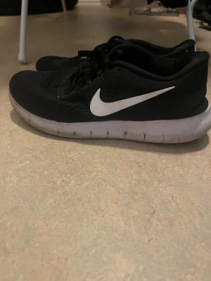 Svarta Nike sneakers med vit sula - Snygga svarta Nike sneakers med vit sula och klassisk vit swoosh på sidan. Ovandelen är i meshmaterial för bra andningsförmåga och skon har en låg profil som ger en sportig look. Perfekta för dig som gillar stilrena och bekväma sneakers.