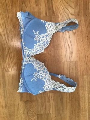 Intimissimi bh gioia - Snygg blå bh med vadderade kupor och dekorativa vita spetsdetaljer i blommönster. Axelbanden är justerbara och bh:n har hakknäppning bak. Materialet är mjukt och bekvämt, perfekt för dig som gillar romantiska detaljer. Bh:n är från Intimissimi i modellen gioia pretty flowers. I mycket bra skick!