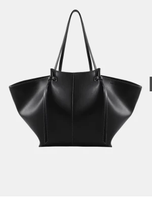 Väska  - Stilren svart shoppingväska i konstläder med vita kontrastsömmar och rymlig design. Väskan har två långa handtag, magnetknäppning och innerfack med dragkedja. Perfekt för dig som vill ha plats för allt och gillar minimalistisk look.