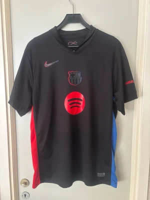 FC Barcelona bortaställ 24/25 - FC Barcelona bortaställ 24/25 matchtröja från Nike. Tryck med Spotify-logga, Champions League märke, klubbmärke och Raphinha 11 på ryggen. 