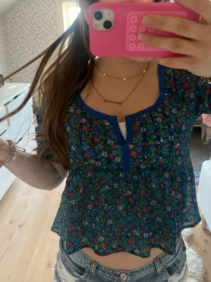 Blommig transparent blus med blå kant - Söt blommig blus i transparent material med blå kant runt halsringningen och knäppning. Sååå söt från hollister i storlek xs, knappt andvänd💗