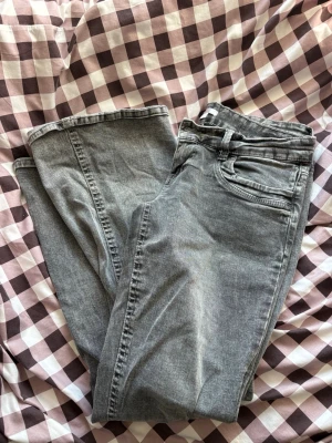 Lågmidjade jeans  - Säljer ett par grå bootcut jeans med låg midja och klassisk femficksdesign. Jeansen har en snygg tvättad look och stängs med knapp och dragkedja. Perfekta till sneakers eller boots för en avslappnad stil. De är stretchiga i materialet.