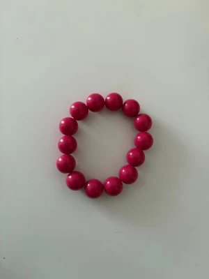 Rosa pärlarmband med stora kulor - Snyggt armband med stora, glansiga rosa pärlor trädda på elastisk tråd. Perfekt för dig som vill ha en färgklick till din outfit. Armbandet har en enkel och stilren design med rundade pärlor i plast.