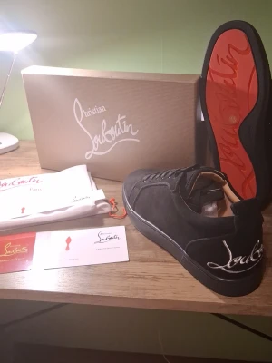 Svarta sneakers från Christian Louboutin - Snygga svarta sneakers från Christian Louboutin med klassisk röd sula och vit logga på hälen. Skorna har en stilren design i mocka och läder, med svarta skosnören och låg profil. Perfekta för dig som vill ha något exklusivt och trendigt. Perfekta skor om du har bal snart!😄💯