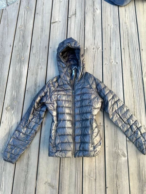 Svart dunjacka med huva McKinley - Snygg svart dunjacka från McKinley i storlek 38. Jackan har quiltad design, dragkedja framtill och en praktisk huva. Superskön!