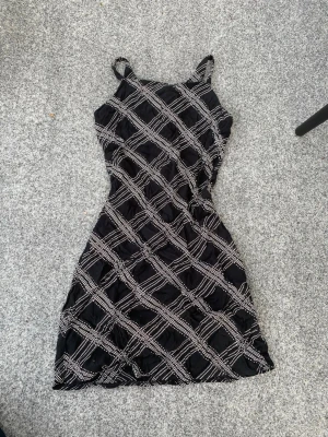 Svart vintage klänning med mönster - Snygg svart kort klänning med smala axelband och ett rutigt mönster i vitt. Klänningen har en figurnära passform och är perfekt för dig som gillar en trendig och vintage stil! Materialet känns mjukt och skönt, nästan som mesh/linne tyg🙌Dragkedja bak. Passar till många tillfällen: fest, begravning, sommarkväll, event, firande osv💕Storlek S. Inga synliga defekter (min mammas gamla från 2000s) men säkert använd några gånger⭐️