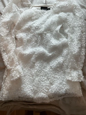 Vit blommig klänning från Pieces - Säljer en vit klänning från Pieces med blommiga detaljer och långärmad design. Har aldrig använt den. 