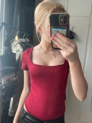 Röd tight topp med fyrkantig ringning - Snygg röd topp med fyrkantig ringning och korta ärmar. Modellen är tight och passar perfekt till både jeans och kjol. Enkel och stilren design utan synliga loggor eller mönster.
