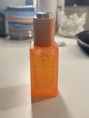 CAIA Summer Drops Tan Serum - CAIA Summer Drops Tan Serum kommer i en orange, fyrkantig plastflaska med pump och silverfärgat lock. Innehåller hyaluronsyra och vitamin E för återfuktning och glow. Perfekt för att ge ansiktet en solkysst ton. Flaskan rymmer 30 ml.