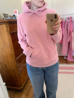 Ljusrosa hoodie med huva - Mysig ljusrosa hoodie med huva och dragsko. Klassisk känguruficka framtill och avslappnad passform. Perfekt för chill dagar eller när du vill ha en enkel och snygg look. Tillverkad i mjukt material som känns skönt mot huden.