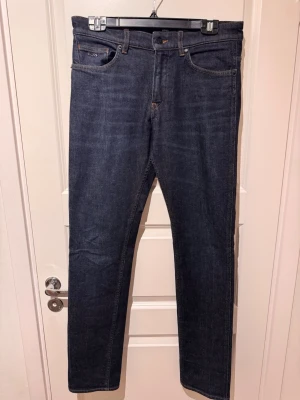 Mörkblå jeans från BOSS - Snygga mörkblå jeans från BOSS med klassisk femficksmodell och raka ben. Jeansen har diskreta kontrastsömmar och en stilren look som passar till det mesta. Tillverkade i bomull för en bekväm känsla hela dagen. Storlek 30 i midja och 32 i längd.