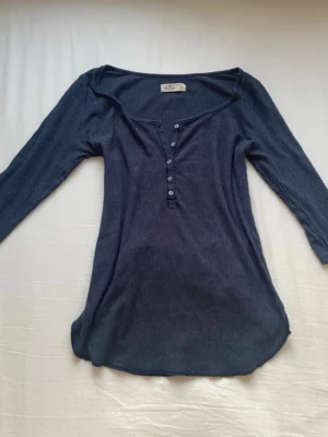 Mörkblå ribbad topp med knappar - Mörkblå ribbad topp med trekvartsärm och v-ringning med knappar framtill. Säljer för att den tyvärr inte passade💗Jättefin till jeans, kjol eller shorts💗💗(lånade bilder)