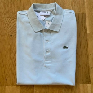 Vit pikétröja från Lacoste - Lacoste Slim Fit Pikétröja i mycket fint skick. Klassisk och stilren modell med smal passform som sitter snyggt på kroppen. Tillverkad i högkvalitativ bomull som är både bekväm och andas bra.   • Storlek: M • Färg: Turkos/Ljusblå • Skick: Mycket bra, oanvänd   • Nypris: ca 1.200 kr • Pris: 600 kr    Skickas samma arbetsdag! Alltid noggrant paketerad. Hör av dig vid frågor och bilder! Smidiga affärer uppskattas alltid.