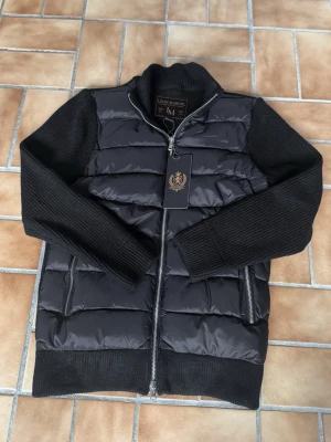 Leon Marcel Hybridjacka – Svart | Klassisk | Ny Med Prislapp - Ny med prislapp — Leon Marcels hybridjacka i tidlös svart med quiltad pufferkropp och stickade ärmar. Lyxiga microfleecefickor som håller händerna varma — detaljer som gör skillnad. Ren och klassisk Skandinavisk design som passar till allt. Perfekt för höst/vinter och kyliga vårdagar. Säljer direkt för ett bättre pris än butik. 📦 Spårad frakt, väl förpackad.