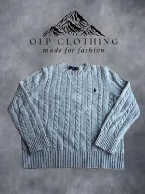 Grå kabelstickad tröja från Polo Ralph Lauren - Säljer en grå kabelstickad tröja från Polo Ralph Lauren med klassisk rund halsringning och svart broderad logga på bröstet. Tröjan har ribbade muddar vid ärmslut och nederkant och är tillverkad i mjukt material som passar perfekt till kyligare dagar. Knappt använd och i riktigt bra skick, qr finns. #12