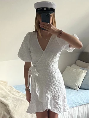 Söt vit omlottklänning - studentklänning - Supersnygg vit omlottklänning med puffärm och volang från Pieces som inte säljs i butik längre!🥰 Passar perfekt till studenten eller sommaren! Helt ny med prislapp kvar😍 Säljer då den aldrig kommit till användning😔