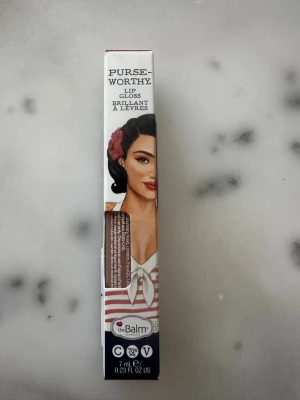 The Balm läppglans brun. Crossbody - Snyggt läppglans från theBalm i nyansen Crossbody. Färgen är en varm brun ton med glansig finish. Förpackningen är på 7 ml och har en retroinspirerad design med illustration. Perfekt för dig som vill ha ett glossigt resultat och en trendig look.