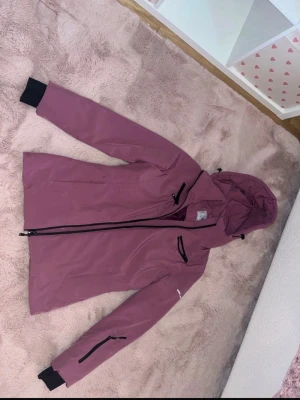 Rosa vindjacka från Cross Sportswear - Snygg rosa vindjacka från Cross Sportswear med huva och svarta detaljer. Jackan har dragkedjor på fickorna, justerbara muddar och en sportig look. Perfekt för blåsiga dagar och outdoor-aktiviteter. Materialet är slitstarkt och vattenavvisande.