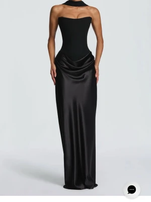 Babyboo Svart axelbandslös satinklänning  - Supersnygg svart lång klänning i satin med axelbandslös design och korsettliv. Klänningen har snörning i ryggen och en draperad midja som ger en lyxig känsla. Perfekt för dig som vill sticka ut med en elegant och modern look. Jättefin till balen eller ett bröllop❤️ jag är 172 cm och har E75 i kupa. Aldrig använt!!