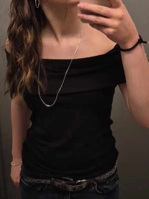 Svart offshoulder topp - Snygg svart offshoulder topp med smickrande passform. Toppen är ärmlös och har en bred kant över axlarna som ger en trendig look. Perfekt att matcha med jeans eller kjol för en cool stil.