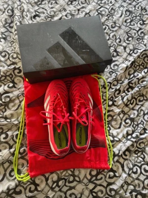 Adidas Predator röda fotbollsskor - Säljer ett par röda Adidas Predator fotbollsskor med vita detaljer och svarta inslag. Skorna har snörning och är designade för bra grepp på planen. Medföljer originalpåse och låda. Perfekta för dig som vill sticka ut på fotbollsplanen. Pris kan diskuteras vid snabb affär och fler bilder kan lösas vid fråga.
