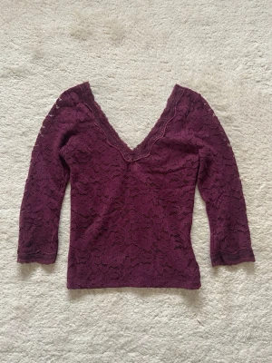 Vinröd spetsblus med v-ringning - Vinröd blus i spets med v-ringning och trekvartsärm. Den är storlek m men sitter som en s. Toppens spetsmaterial ger en elegant look och den har en figurnära passform. Perfekt att styla med jeans eller kjol.