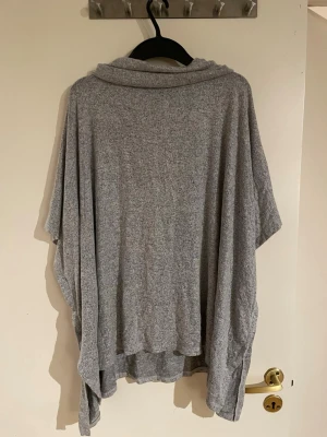 Grå oversized cardigan med krage - Mysig gråmelerad oversized cardigan med lös passform och bred krage. Tillverkad i mjukt, tunt stickat material som faller snyggt. Perfekt att slänga över en t-shirt eller topp för en chill look.