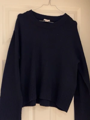 Blå stickad tröja med ribbad kant - En blå stickad tröja med rund hals och ribbstickade muddar vid ärmslut och nederkant. Tröjan har en något boxig och kortare passform, perfekt för att matcha med jeans eller kjol. Materialet är mjukt och tjockt, vilket gör den extra bekväm.