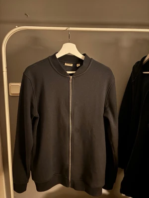 Svart zip hoodie från Only & sons - En stilren svart hoodie från  Only & sons med dragkedja framtill och ribbade muddar vid ärmslut och nederkant. Klassisk passform utan tryck eller mönster, perfekt till vardags. Tillverkad i mjukt sweatshirtmaterial för skön känsla.