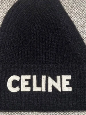 Celine mössa - Svart ribbstickad mössa från Celine med klassisk broderad logga framtill. Mössan har en bred uppvikt kant och är gjord av ull som håller en varm med bekväm passform.  Pris kan diskuteras, tveka ej att skriva vid frågor!