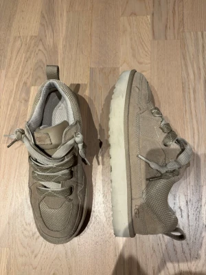 Low Mel UGG - Snygga beige sneakers från UGG med robust sula och coola detaljer. Skorna har en mix av mocka och mesh, breda snören och dragflik bak. Perfekta för dig som gillar streetwear och vill ha något bekvämt och stilrent. Passar 41-42.