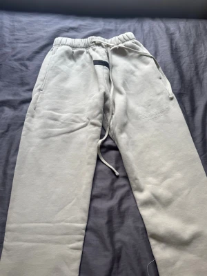 Beige mjukisbyxor från Essentials - Säljer ett par beige mjukisbyxor från Essentials Fear of God. Byxorna har dragsko i midjan, muddar vid bensluten och två sidofickor. Tillverkade i mjukt och fleecefodrat material för extra komfort. Perfekta för chill dagar eller när du vill vara extra bekväm.