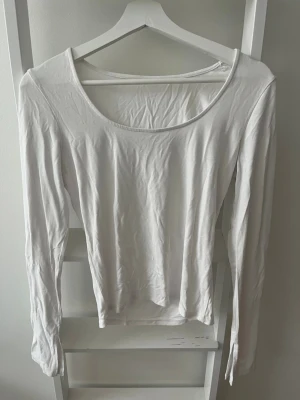 Vit långärmad topp med slits - En enkel och stilren vit långärmad topp med square halsringning och slitsdetalj vid ärmsluten. Perfekt att matcha med jeans eller kjol för en clean look. Tillverkad i mjuk bomull för skön känsla hela dagen. Från Gina Tricot. Köparen står för eventuell frakt.