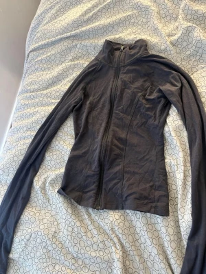 Svart sportjacka med dragkedja - Slimmad svart sportjacka med hel dragkedja framtill och hög krage. Tillverkad i ett stretchigt och lätt material som passar perfekt för träning eller löpning. Långa ärmar och figurnära passform ger en sportig look.