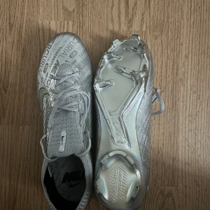 Nike Mercurial Limited Edition i Silver - Säljer ett par Nike Mercurial fotbollsskor i metallic silver med guldigt märke på sidan. Skorna har snörning och mönstrad ovandel med textdetaljer. Yttersulan är i blankt silver med fasta dobbar, perfekt för spel på gräs och konstgräs!