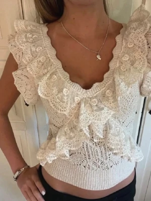 Vit spetsblus med volanger - Supersöt vit blus med spetsdetaljer och volanger längs v-ringningen och ärmarna. Kortärmad och croppad modell med ribbad midja och romantisk känsla. Perfekt för dig som gillar feminina och trendiga toppar.