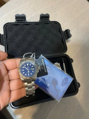 Blå dykarklocka från Addiesdive - Snygg dykarklocka från Addiesdive med blå urtavla och silverfärgat armband i rostfritt stål. Klockan har tydliga markeringar, datumfönster och vridbar bezel. Kommer i originalbox med extra länkar och verktyg.Den kostar igentligen 1000kr