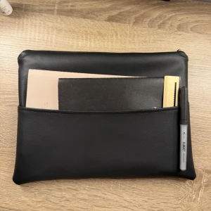 Svart datorväska i konstläder - Slimmad svart datorväska i konstläder med en stor ytterficka för block, linjal och penna. Väskan har minimalistisk design och dragkedja upptill. Perfekt för att bära laptop och tillbehör till plugget eller jobbet.