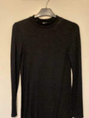 Svart långärmad polotopp - En klassisk svart långärmad polotopp med halvhög hals. Perfekt att styla till olika outfits och funkar året runt. Enkel och stilren design som passar till det mesta.